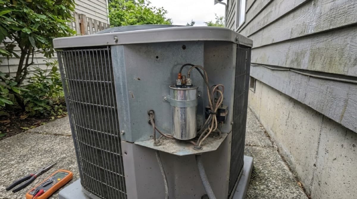 HVAC technician in Burbank California kneeling beside an outdoor AC condenser unit checking refrigerant pressure with manifold gauges during a summer service call